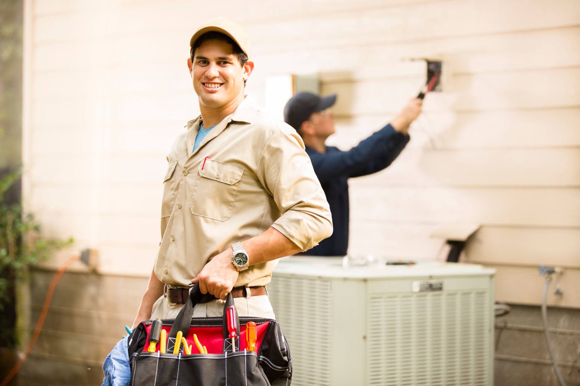 Air conditioner repairmen work on home unit. Blue collar workers.